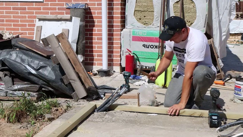 В случае с фундаментом-плитой обвязочный брус, то есть самые первые четыре доски, кладут на гидроизоляцию и закрепляют анкерами — это специальные болты, который проходят брус и заходят в плиту. Длина анкера около 15 см, под них надо самостоятельно высверлить отверстия перфоратором