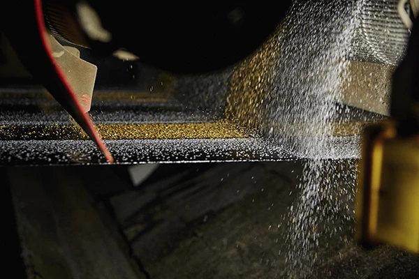 После нанесения гранул полотно проходит через прикаточный вал — это нужно, чтобы они плотно сцепились и спрессовались, превратившись в единое покрытие.