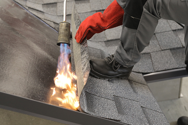 При укладке первого ряда гибкой черепицы надо промазать мастикой карнизную и торцевую планку на 100 мм. Потом, прогревая ковер, укладывайте гонт за гонтом. При этом горелку направляйте исключительно на подкладочный ковер, а не на гибкую черепицу. Прикатывайте каждый гонт роликом, слегка утапливая. На коньке гонты последнего ряда подрежьте по размеру, но не наплавляйте, а прикрепите саморезами с шагом 150 мм.